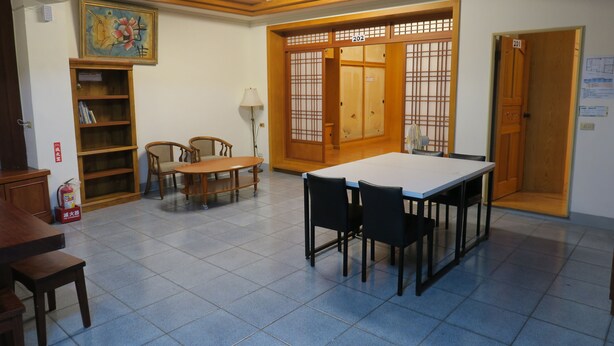 A room with a dining table, chairs, a bookshelf, a lamp, and a traditional Japanese sliding door.