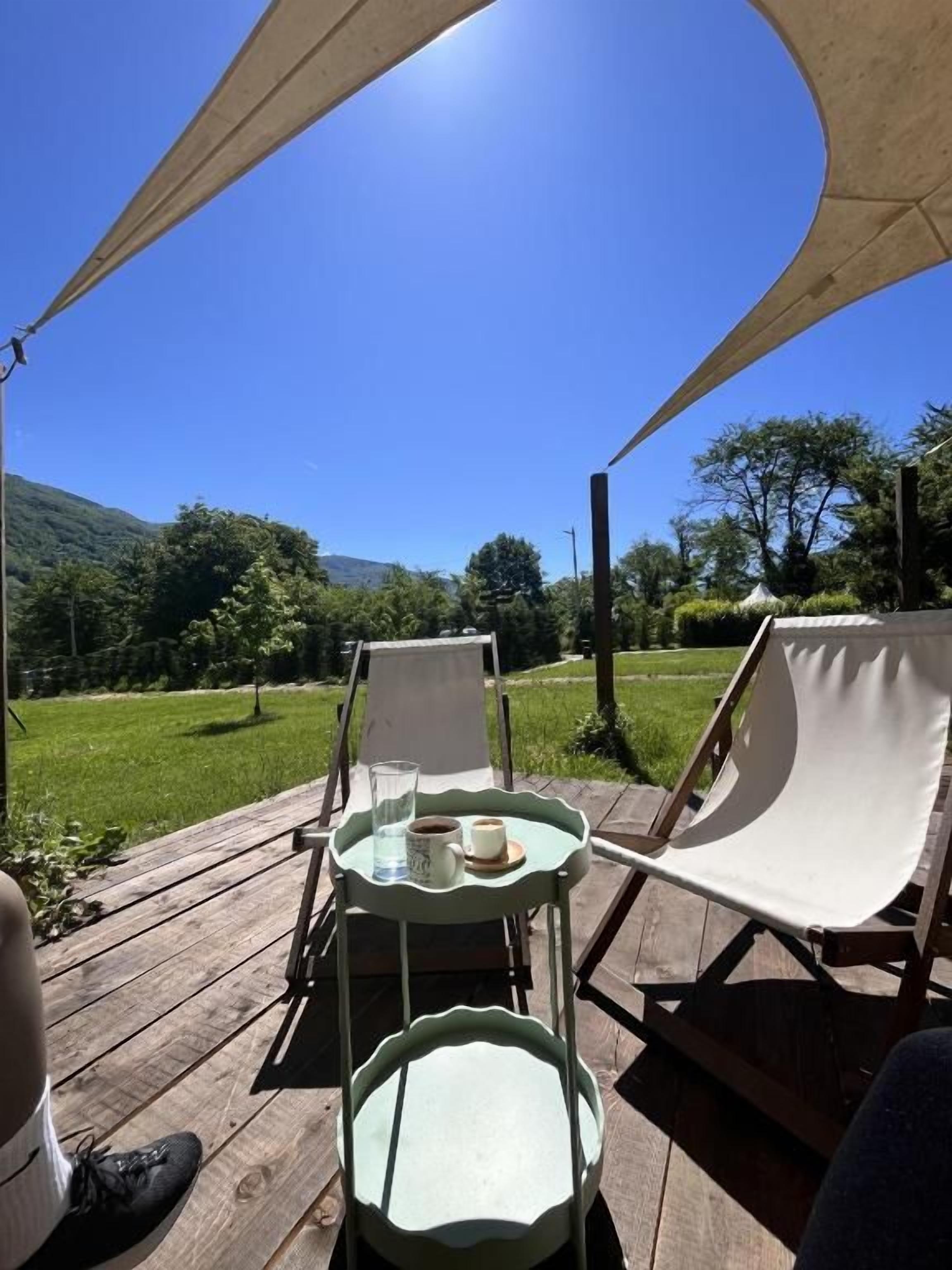 Un espace extérieur aménagé avec une table et des chaises, installé sous une tonnelle, et offrant une vue sur un paysage verdoyant, avec des arbres et des collines.
