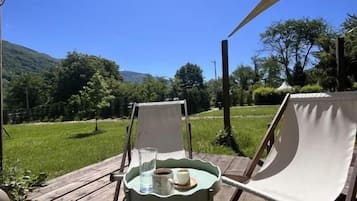 Un espace extérieur aménagé avec une table et des chaises, installé sous une tonnelle, et offrant une vue sur un paysage verdoyant, avec des arbres et des collines.