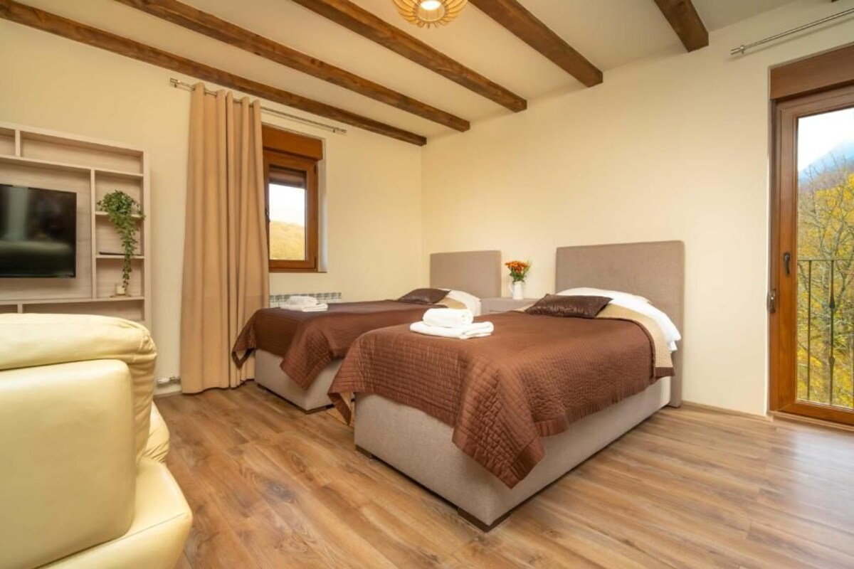 A hotel room with two beds, a TV, a sofa, and a window with a view.