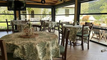 Un espace repas comprenant plusieurs tables et chaises, de grandes fenêtres et un plafond en bois.