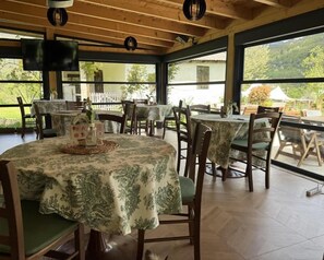 A dining area with multiple tables and chairs, large windows, and a wooden ceiling. - Zvjezdana dolina Garni hotel & Glamping (Andrijevica Municipality)