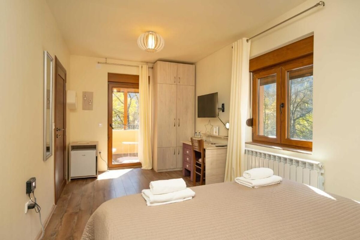 A bedroom with a bed, a desk, a chair, a television, and a window.