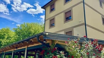 Un immeuble à plusieurs étages doté d’un espace extérieur couvert avec des sièges et d’un jardin agrémenté de plantes à fleurs.