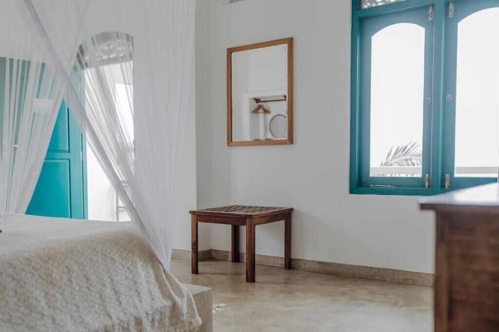 A room with a bed, a small wooden table, a mirror, and a window with a view.