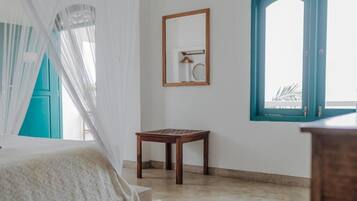 A room with a bed, a small wooden table, a mirror, and a window with a view.