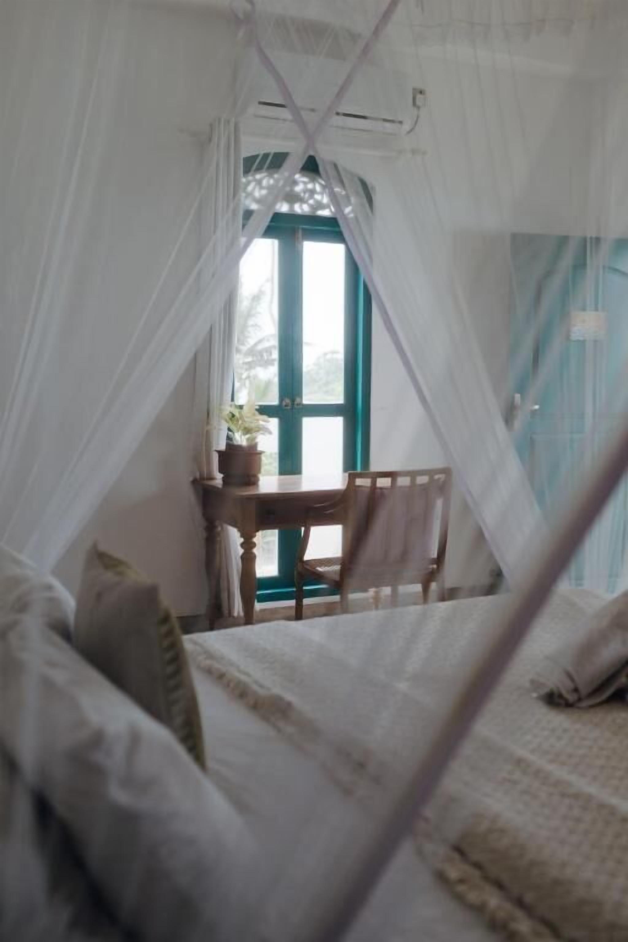Una habitación con una cama bajo un dosel, un escritorio con una silla y una ventana con vistas.