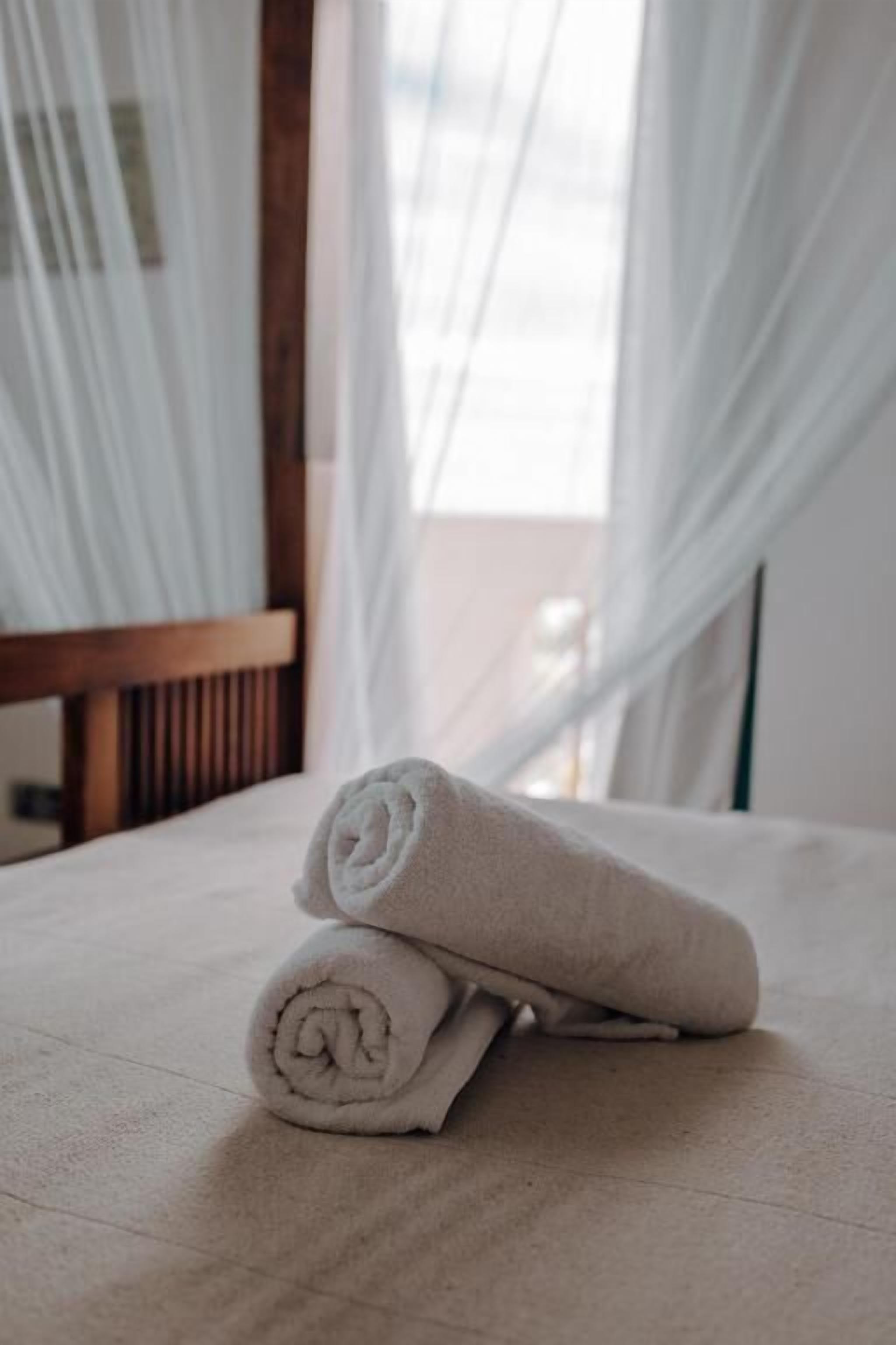 Una cama con toallas blancas enrolladas y cortinas de lino blanco.