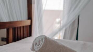 A bed with rolled white towels and sheer white curtains.