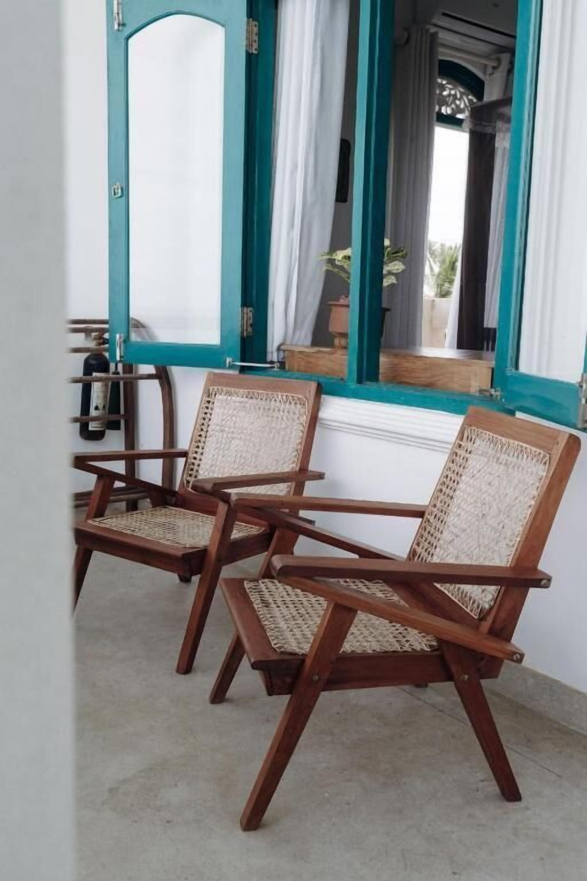 A room with two wooden chairs with woven seats, a window with teal trim, and a view of the outside.