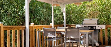 An outdoor patio with a wooden deck, a grill, and a table with chairs.