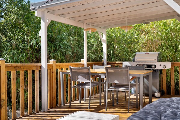 Une terrasse extérieure avec une plateforme en bois, un barbecue et une table avec des chaises.