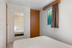 Une chambre à coucher avec un lit, une armoire en bois, un miroir et une fenêtre avec des rideaux.