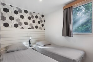 A bedroom with two beds, a geometric wall pattern, a window with curtains, and a bedside lamp. - Bungalow “L’échappée” with Mountain View, Wi-Fi, and Air Conditioning (Saint-Alban-Auriolles)