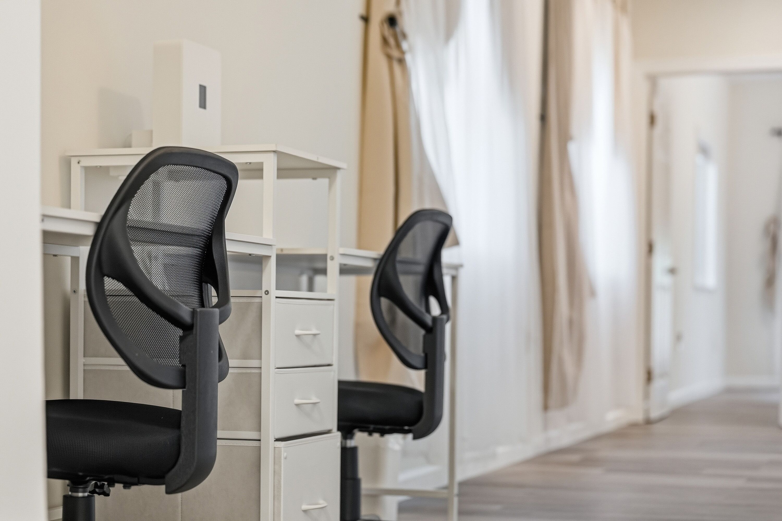 A row of office chairs with mesh backs and black seats, aligned with white filing cabinets.
