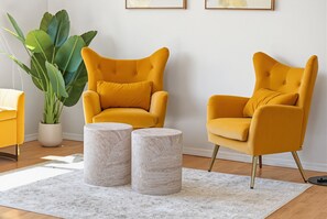 Ein Zimmer mit zwei gelben Sesseln, einer großen Grünpflanze und zwei Marmortischen.