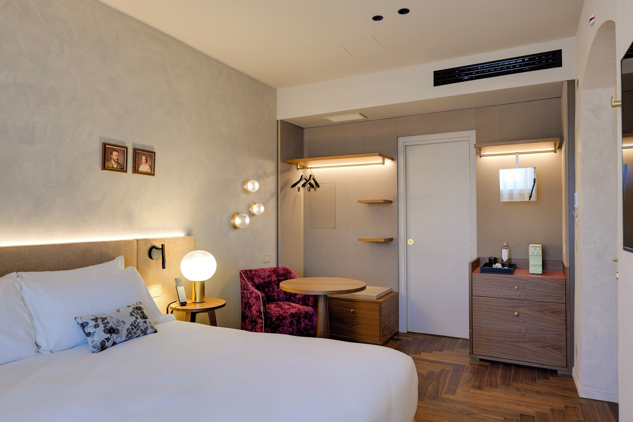 A hotel room with a bed, a chair, a small table, a dresser, and a door.