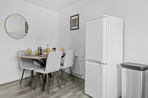 Une cuisine moderne avec un réfrigérateur blanc, une table à manger avec des chaises et un miroir fixé au mur.