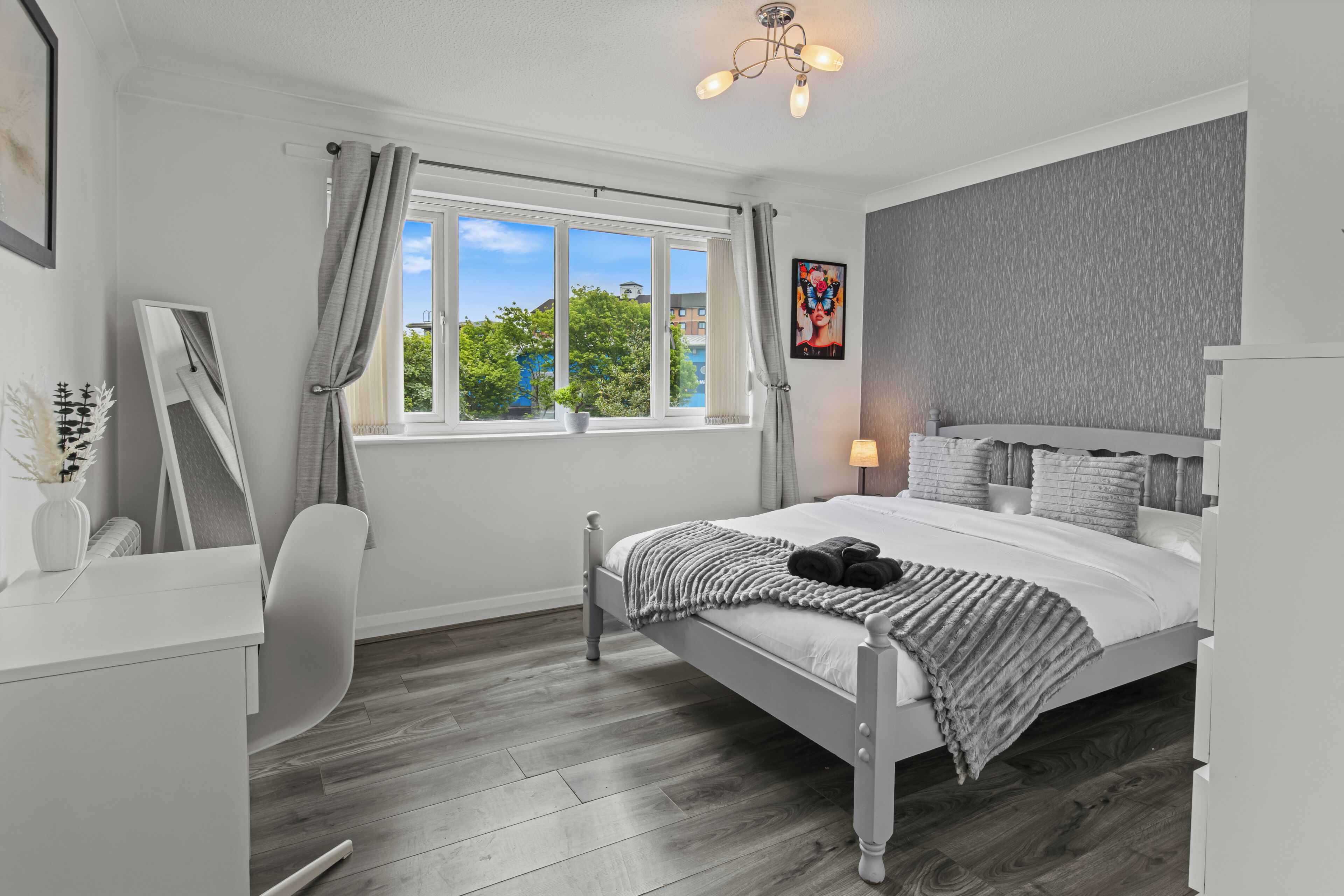Un dormitorio con cama, mesita de noche, lámpara y ventana con cortinas.