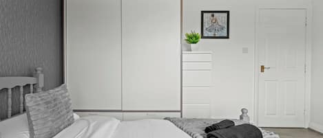 A bedroom with a bed, a wardrobe, a small potted plant, a framed picture, and a door.
