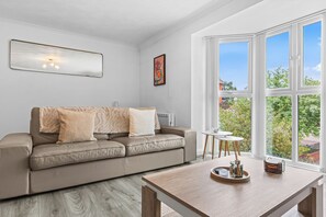 Ein modernes Wohnzimmer mit einer Ledersofa, einem Couchtisch und einem großen Fenster mit Blick auf Grünflächen.