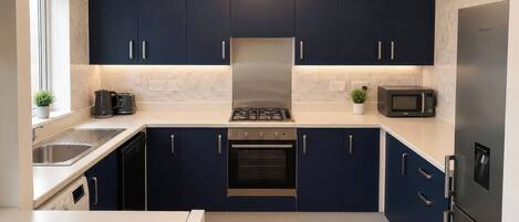 A modern kitchen with dark blue cabinets, a stainless steel range hood, a built-in oven, a microwave, and a dishwasher.