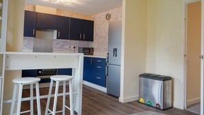 A compact kitchen with dark cabinets, a microwave, a refrigerator, and a trash bin. - 4 Britannia Street (Salford)