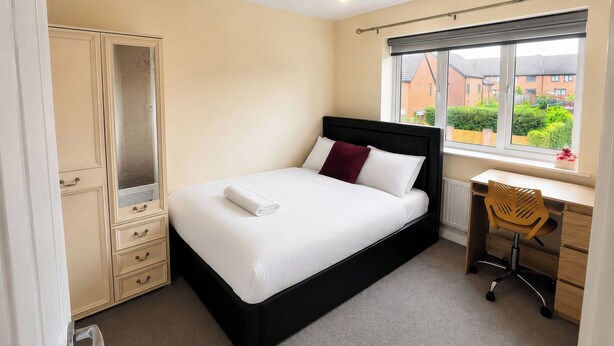 A bedroom with a bed, a desk, a chair, a wardrobe, and a window with a view of buildings. - 4 Britannia Street (Salford)