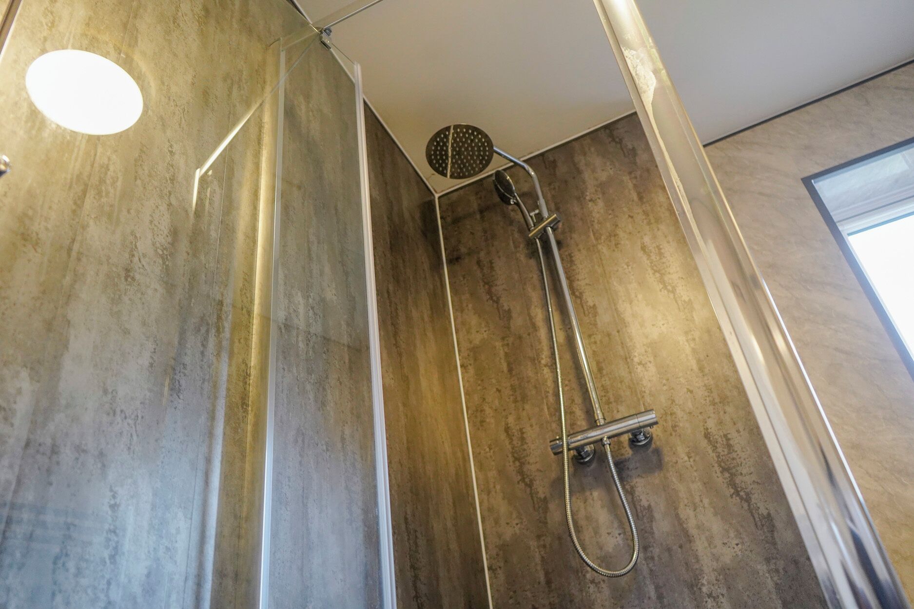 A shower with a handheld showerhead and a wall-mounted control panel.