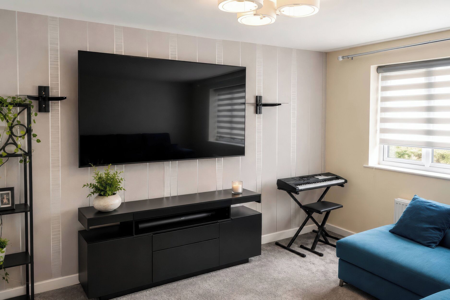 Un salon moderne doté d’un grand téléviseur à écran plat fixé au mur, d’un meuble de rangement noir, d’un canapé bleu et d’une fenêtre avec des stores.