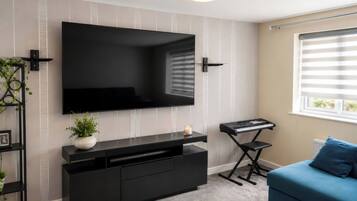 Un salon moderne doté d’un grand téléviseur à écran plat fixé au mur, d’un meuble de rangement noir, d’un canapé bleu et d’une fenêtre avec des stores.