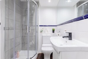 Ein modernes Badezimmer mit einer gläsernen Duschkabine, einer weißen Toilette und einem Waschbecken mit Spiegel darüber.