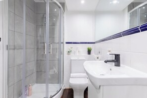 A modern bathroom with a glass-enclosed shower, a white toilet, and a sink with a mirror above. - Charmingly Curated 1BD Flat in the Heart of Fulham (London)