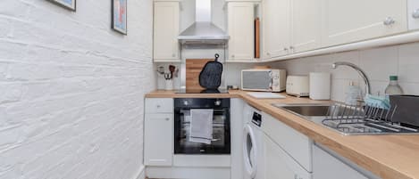 A compact kitchen with white cabinetry, a built-in oven, a microwave, and a sink with a dish rack.