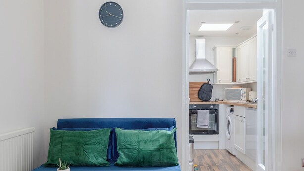 Ein gemütlicher, kleiner Wohnbereich mit blauem Sofa, einem runden Tisch und einer Küchenzeile mit Mikrowelle und Toaster.