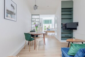 A modern living room with a dining area, a TV mounted on the wall, and a staircase leading to an upper level. - Charmingly Curated 1BD Flat in the Heart of Fulham (London)