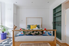 Ein Schlafzimmer mit einem Bett, einem Holz-Kopfteil, einem grünen Kleiderschrank und einer Zimmerpflanze.