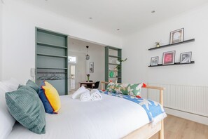 A bedroom with a bed, a bedside table, a chair, and a shelf with pictures. - Charmingly Curated 1BD Flat in the Heart of Fulham (London)