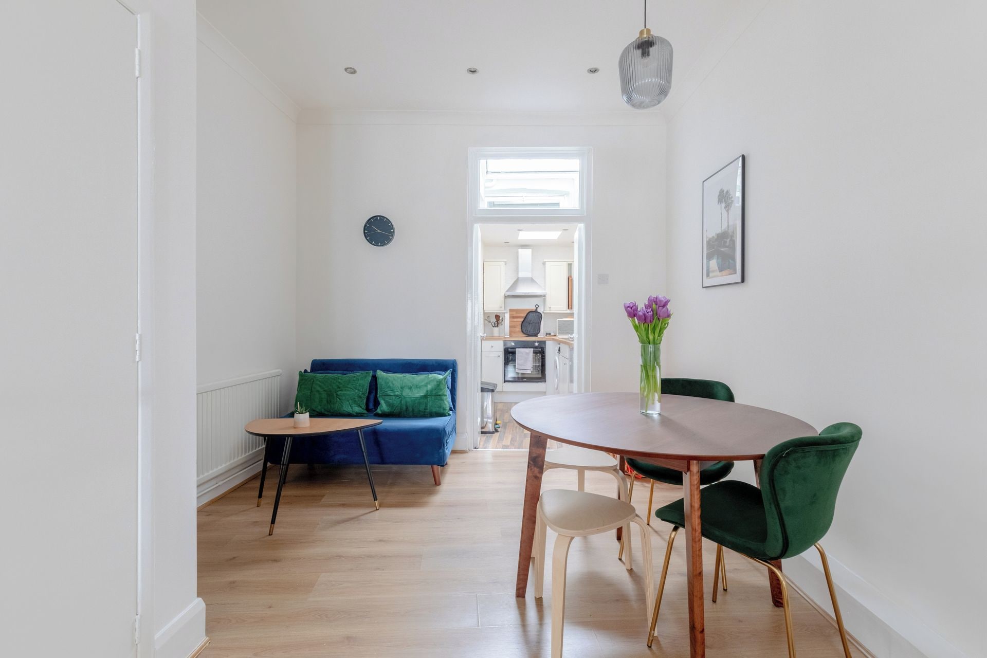 Un salon moderne avec un canapé bleu, une table à manger en bois et des chaises, et une cuisine en arrière-plan.