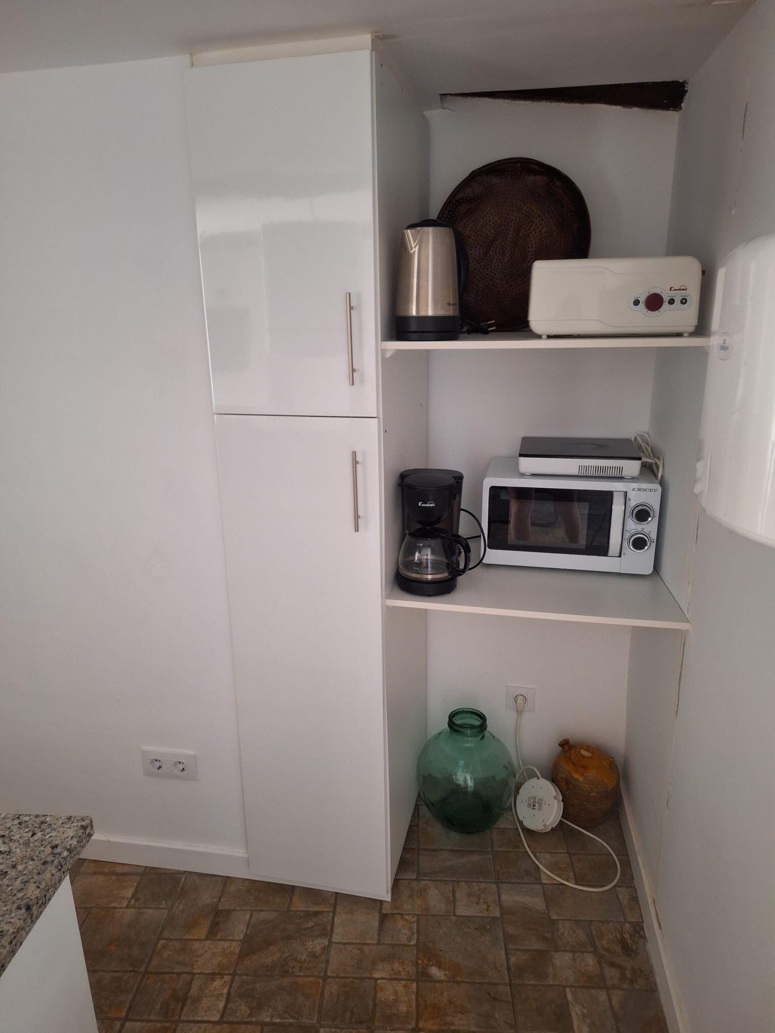 Een kleine keuken met een witte koelkast, een koffiezetapparaat, een magnetron en een broodrooster op het aanrecht.