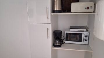 Een kleine keuken met een witte koelkast, een koffiezetapparaat, een magnetron en een broodrooster op het aanrecht.