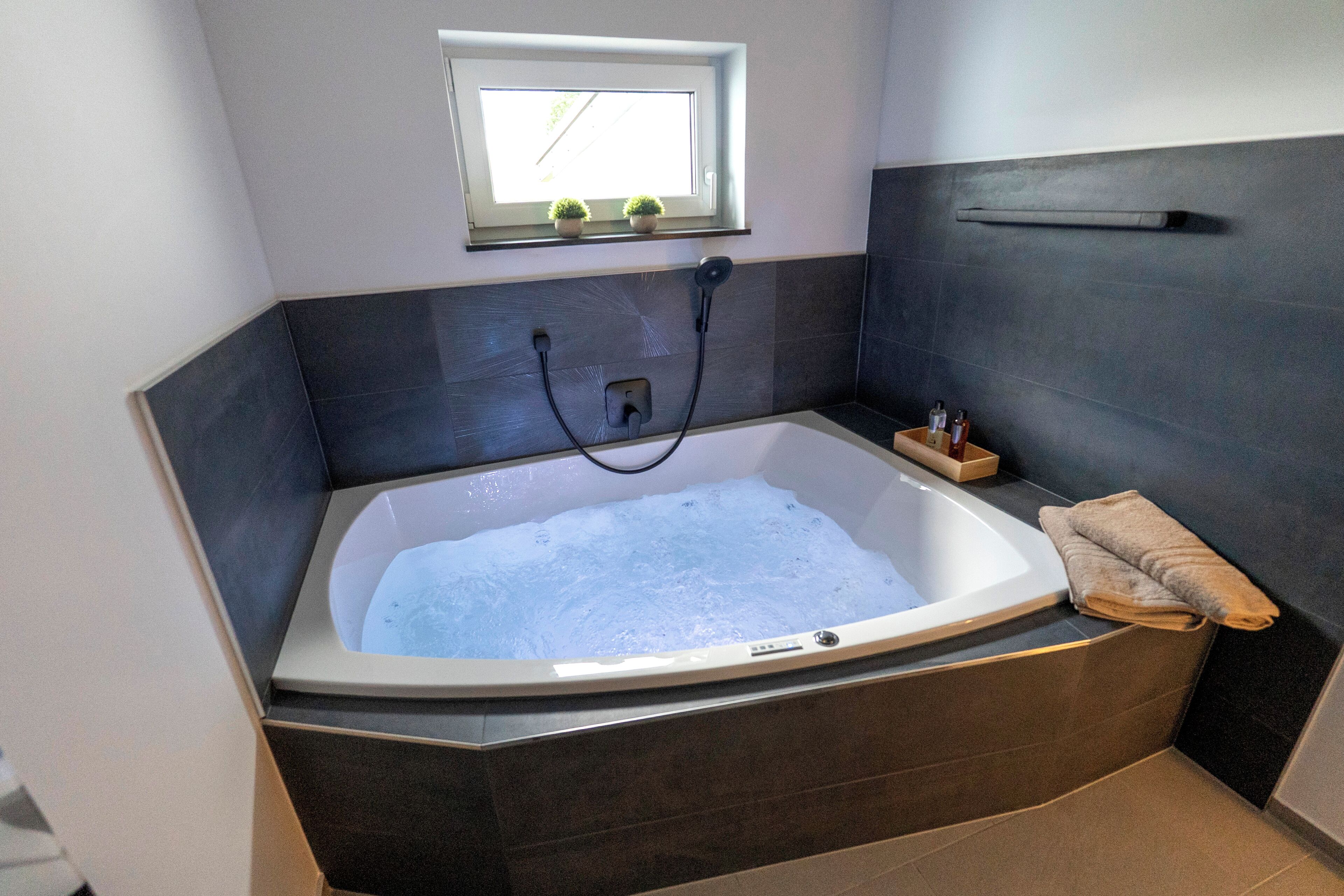 A modern bathroom with a freestanding bathtub, a small window with plants, and a towel rack.
