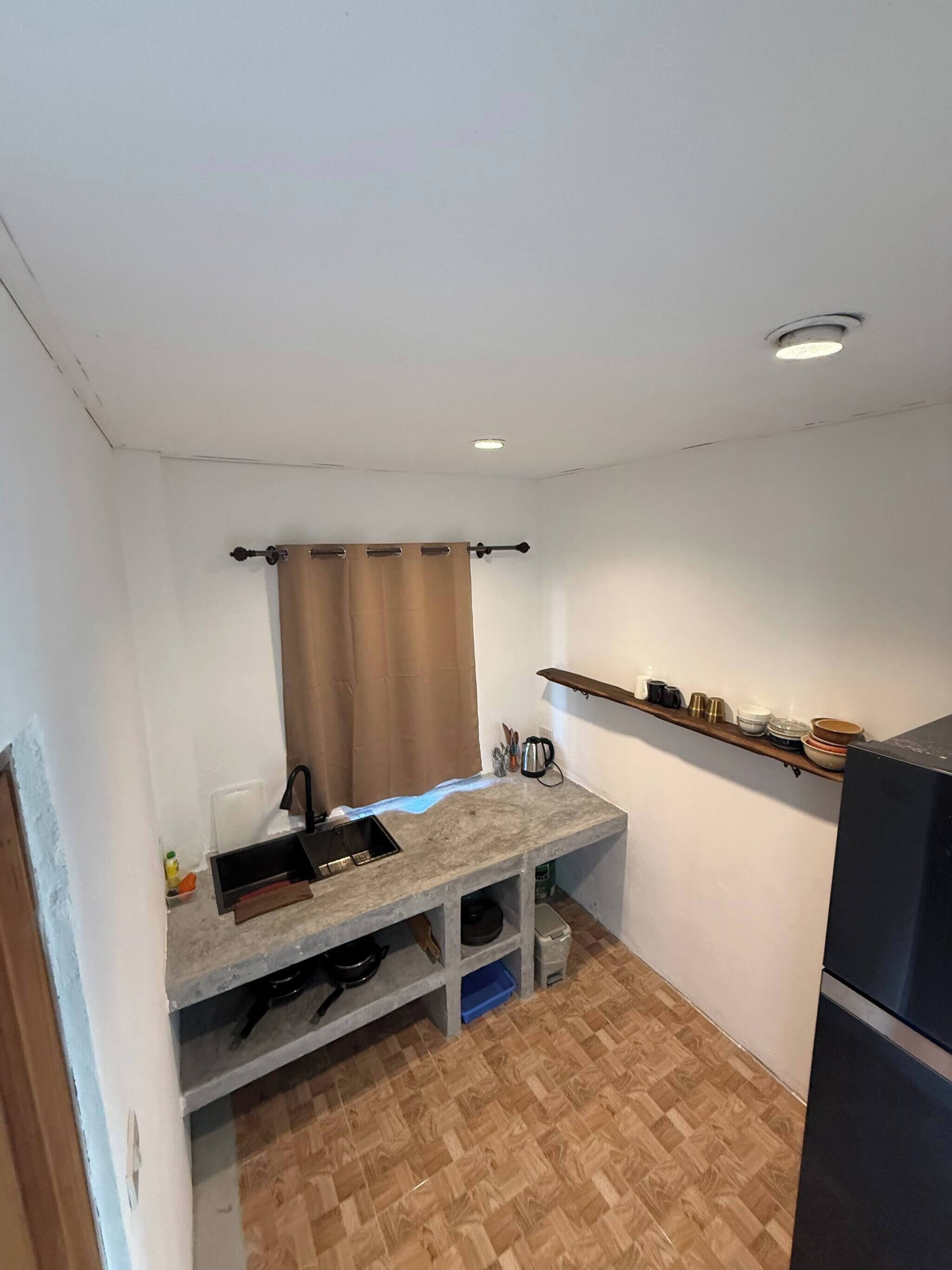 Una cucina compatta con lavandino, piano di lavoro, pavimento in legno ed un ripiano a muro con stoviglie.