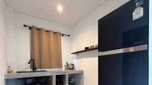 Una cocina compacta con refrigerador integrado, una ventana con cortina y piso de madera.