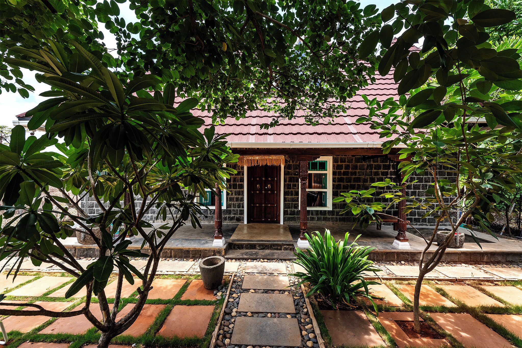 A traditional house with a tiled roof, a stone pathway leading to the entrance, and lush greenery surrounding the property.