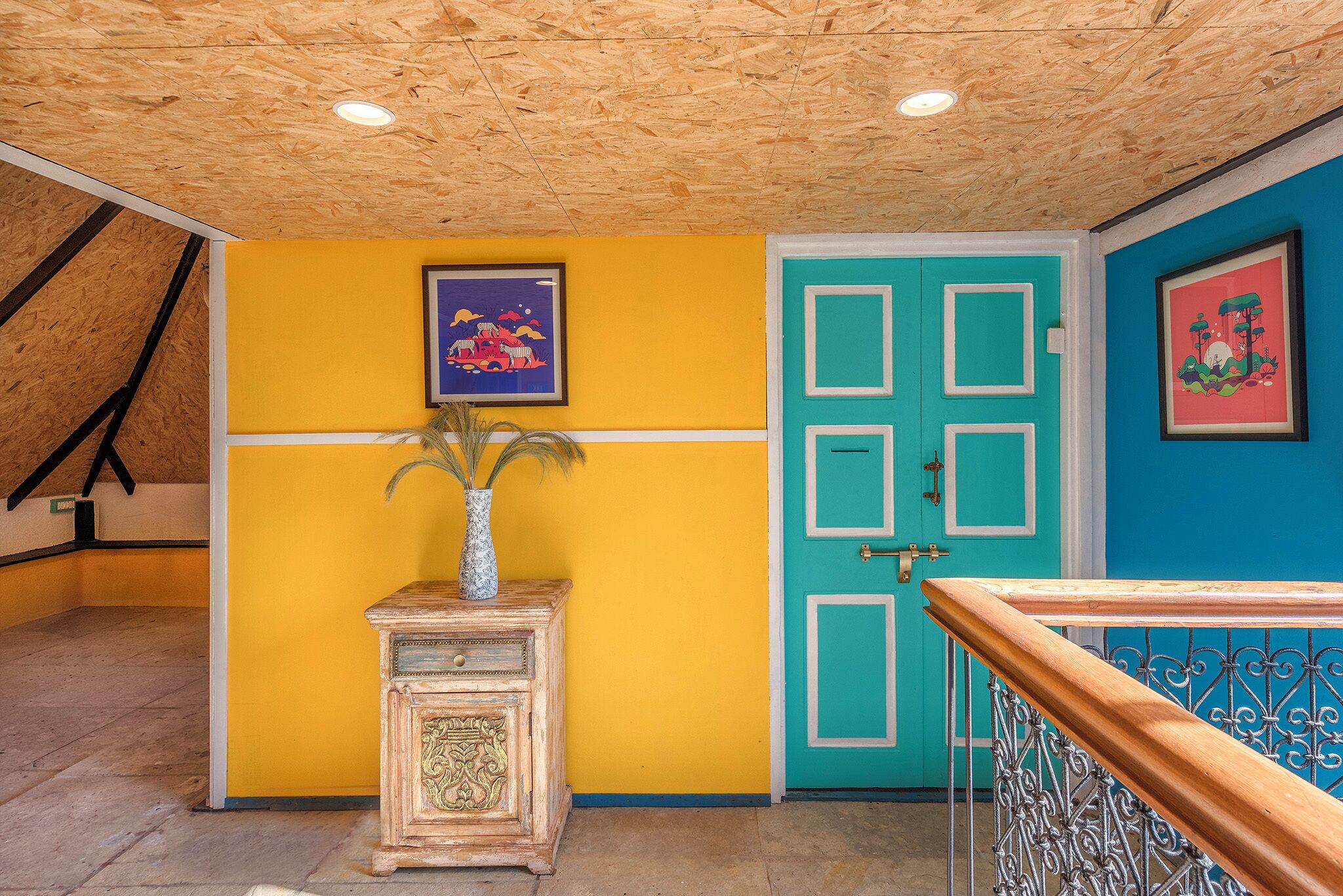 Um quarto com teto de madeira, parede amarela, porta azul-turquesa e um quadro emoldurado acima da porta.