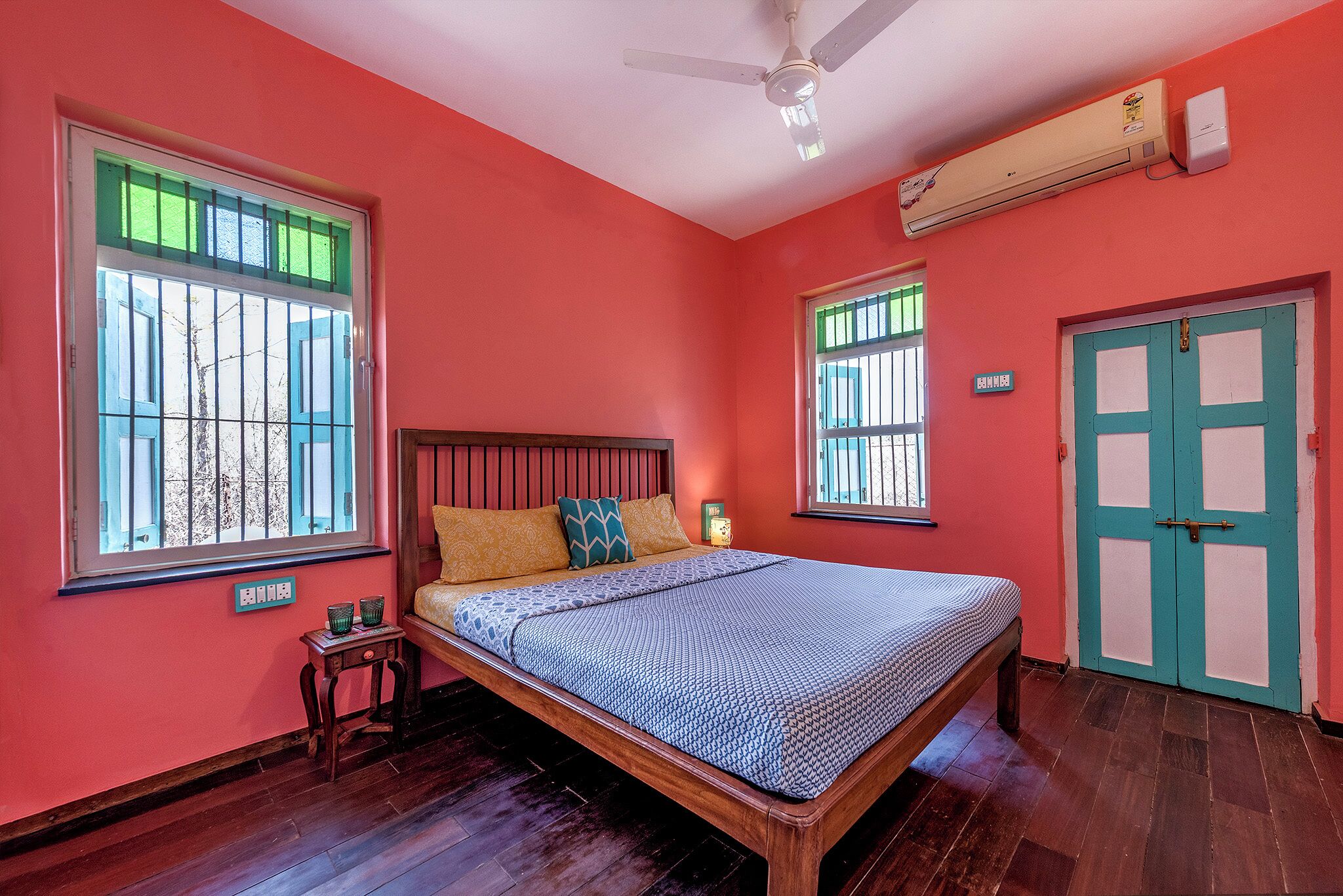 A bedroom with a bed, two windows, a ceiling fan, and an air conditioning unit.