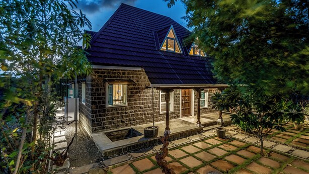 Uma casa de pedra com telhado escuro, varanda e um pequeno jardim.