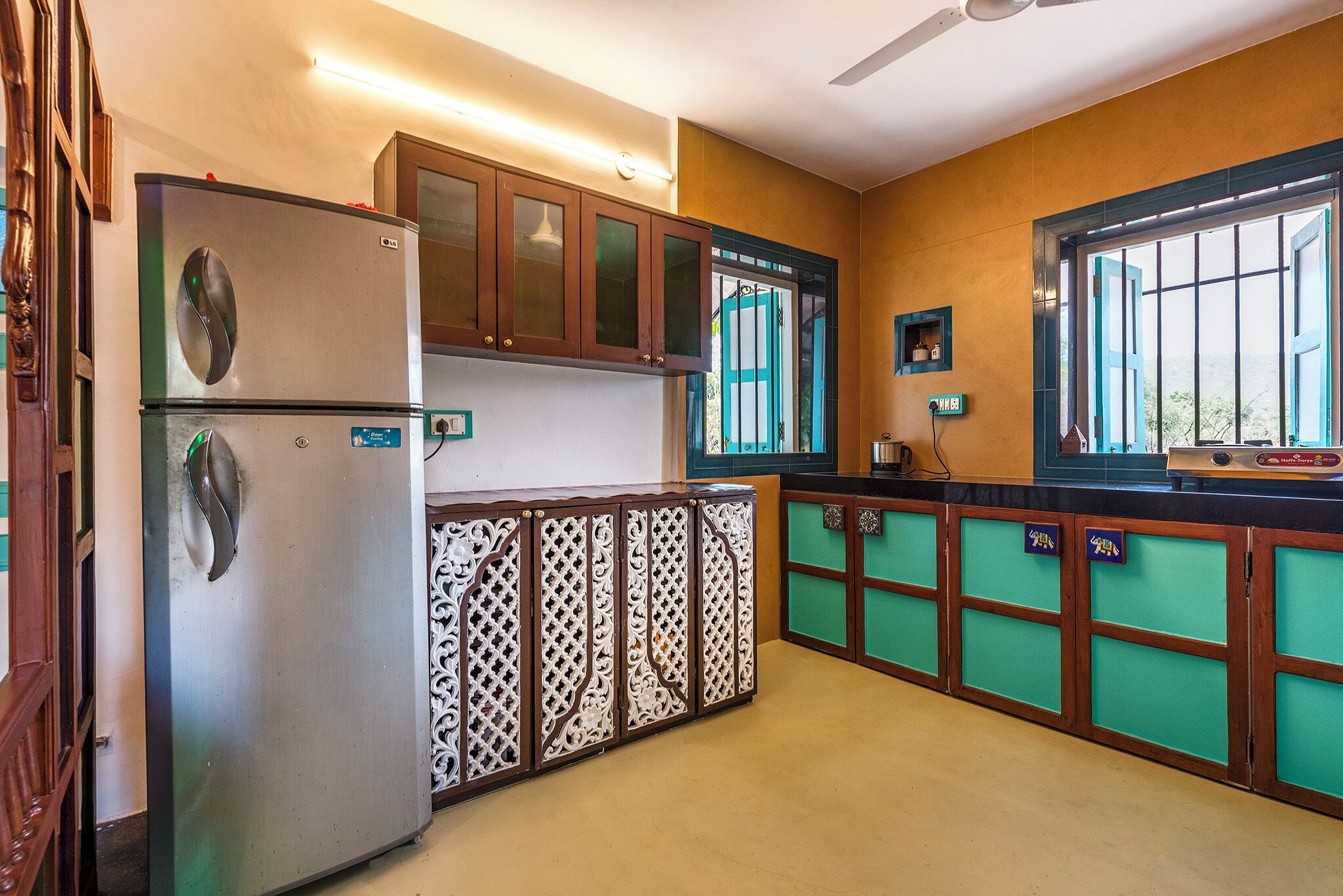 A kitchen with a refrigerator, wooden cabinets, a window with bars, and a green counter.