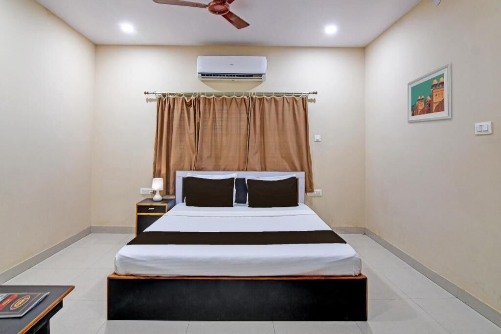 A bedroom with a bed, an air conditioner, a ceiling fan, a nightstand, a lamp, and a framed picture on the wall.